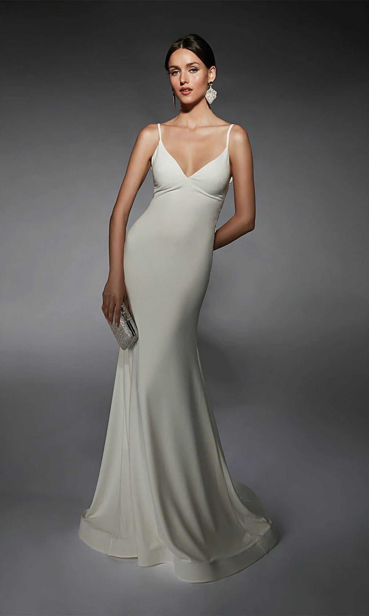 A woman in the Alyce 7108 long ivory dress poses against a dark background, holding a silver clutch and wearing statement earrings.